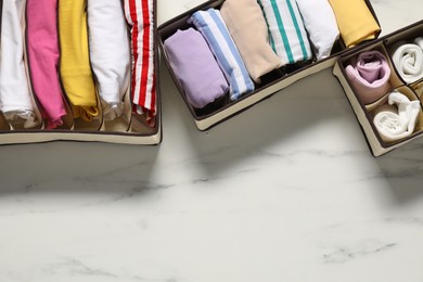 Photo of Organizers with folded clothes on white marble table, flat lay. Space for text