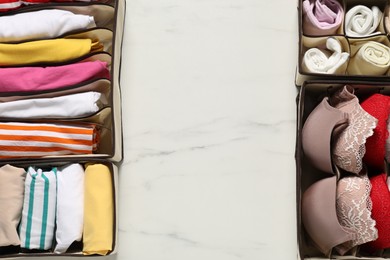 Photo of Organizers with folded clothes and underwear on white marble table, flat lay. Space for text