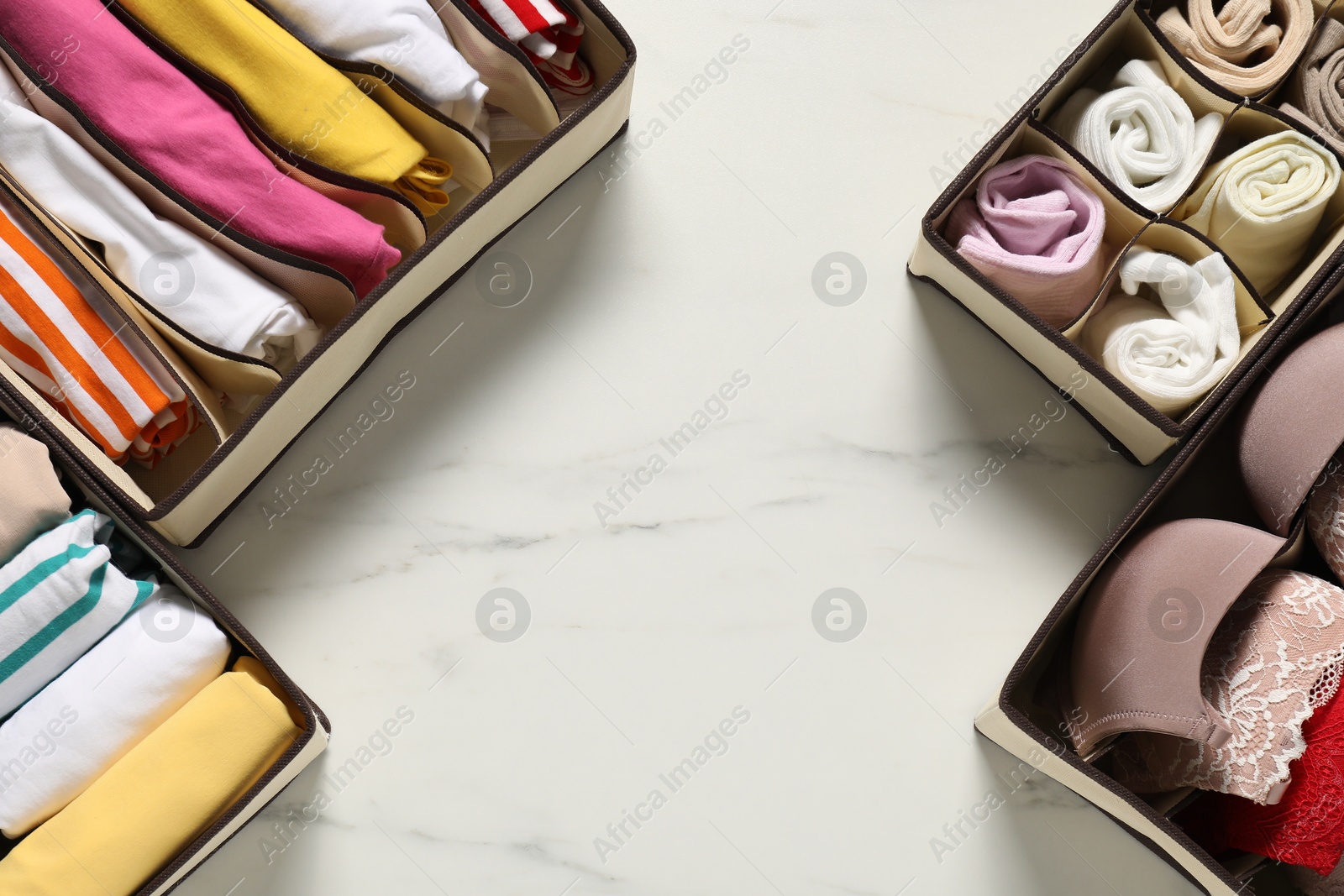 Organizers with folded clothes and underwear on white marble table, flat lay. Space for text Photo of Organizers with folded clothes and underwear on white marble table, flat lay. Space for text