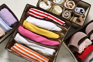 Photo of Organizers with folded clothes and underwear on white marble table, flat lay