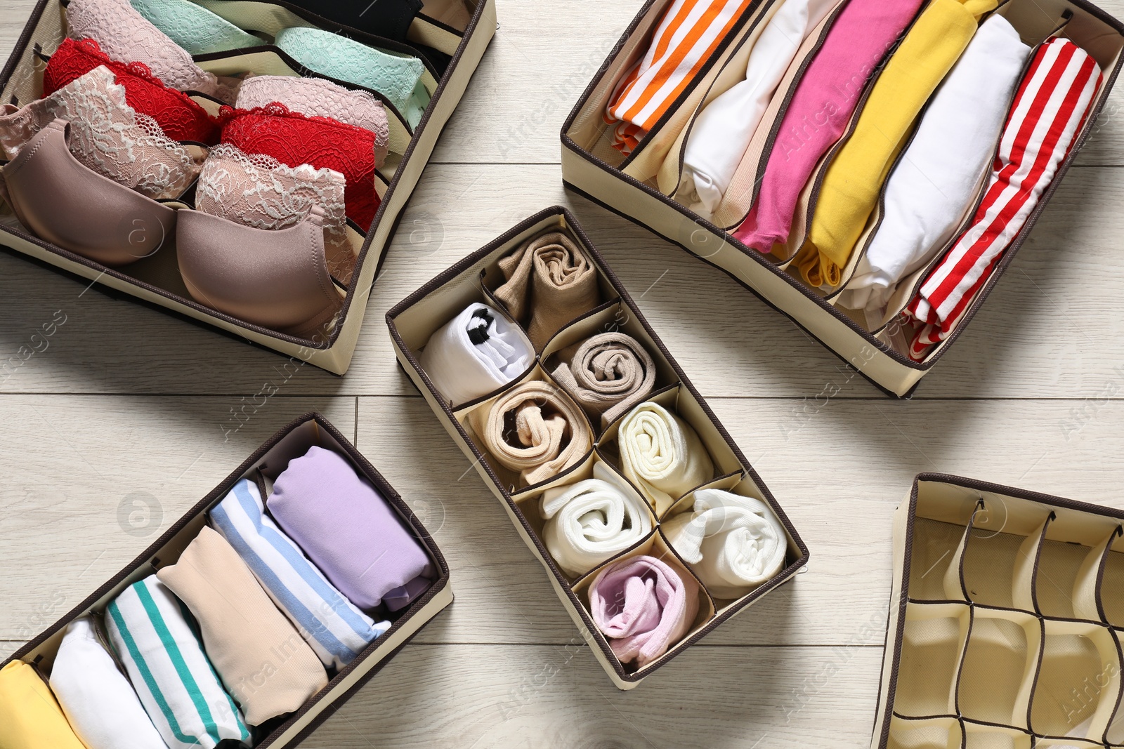 Organizers with folded clothes and underwear on wooden floor, flat lay Photo of Organizers with folded clothes and underwear on wooden floor, flat lay