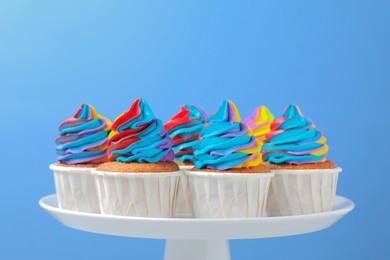 Tasty cupcakes with colorful cream on light blue background, closeup