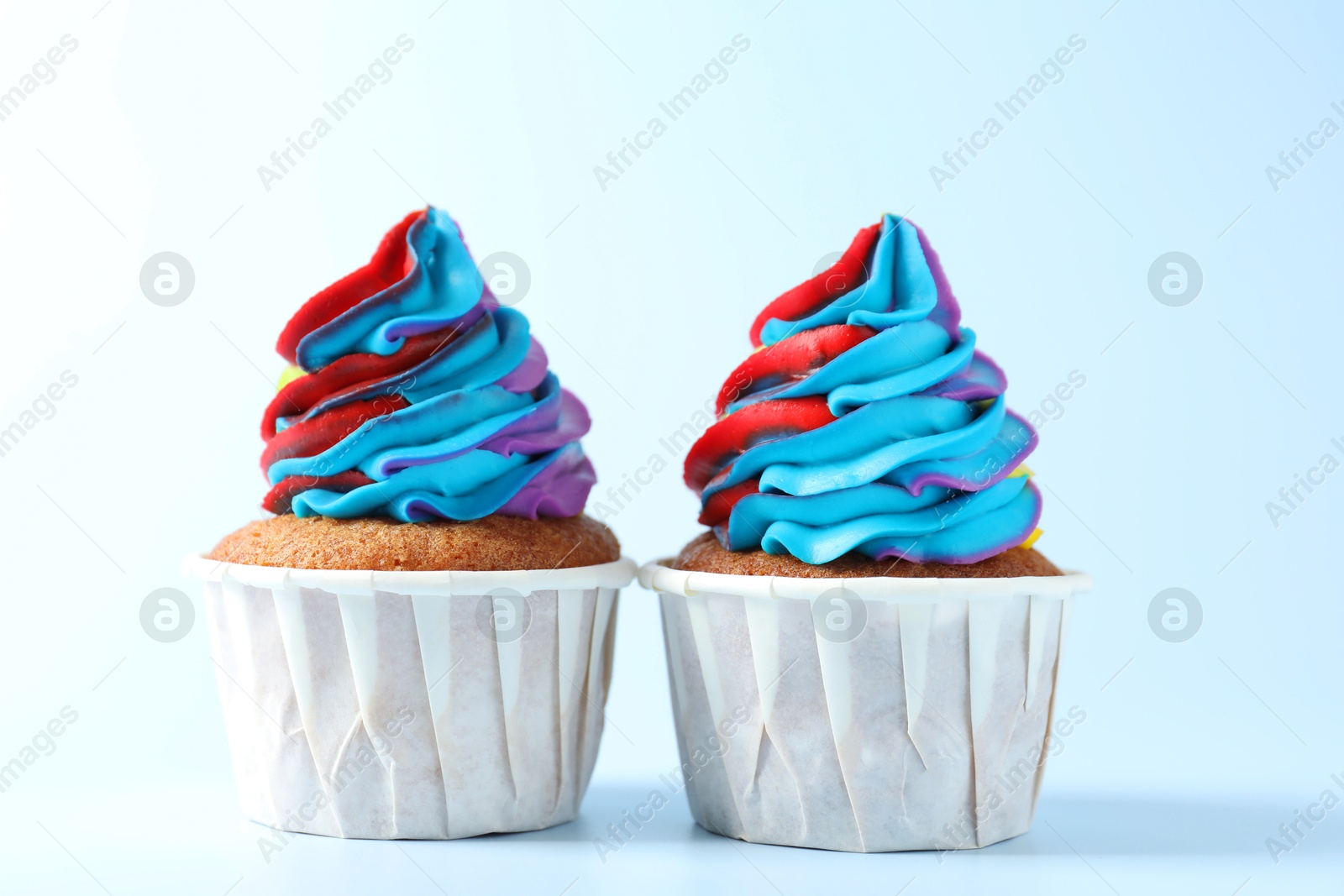 Photo of Tasty cupcakes with colorful cream on light blue background, closeup