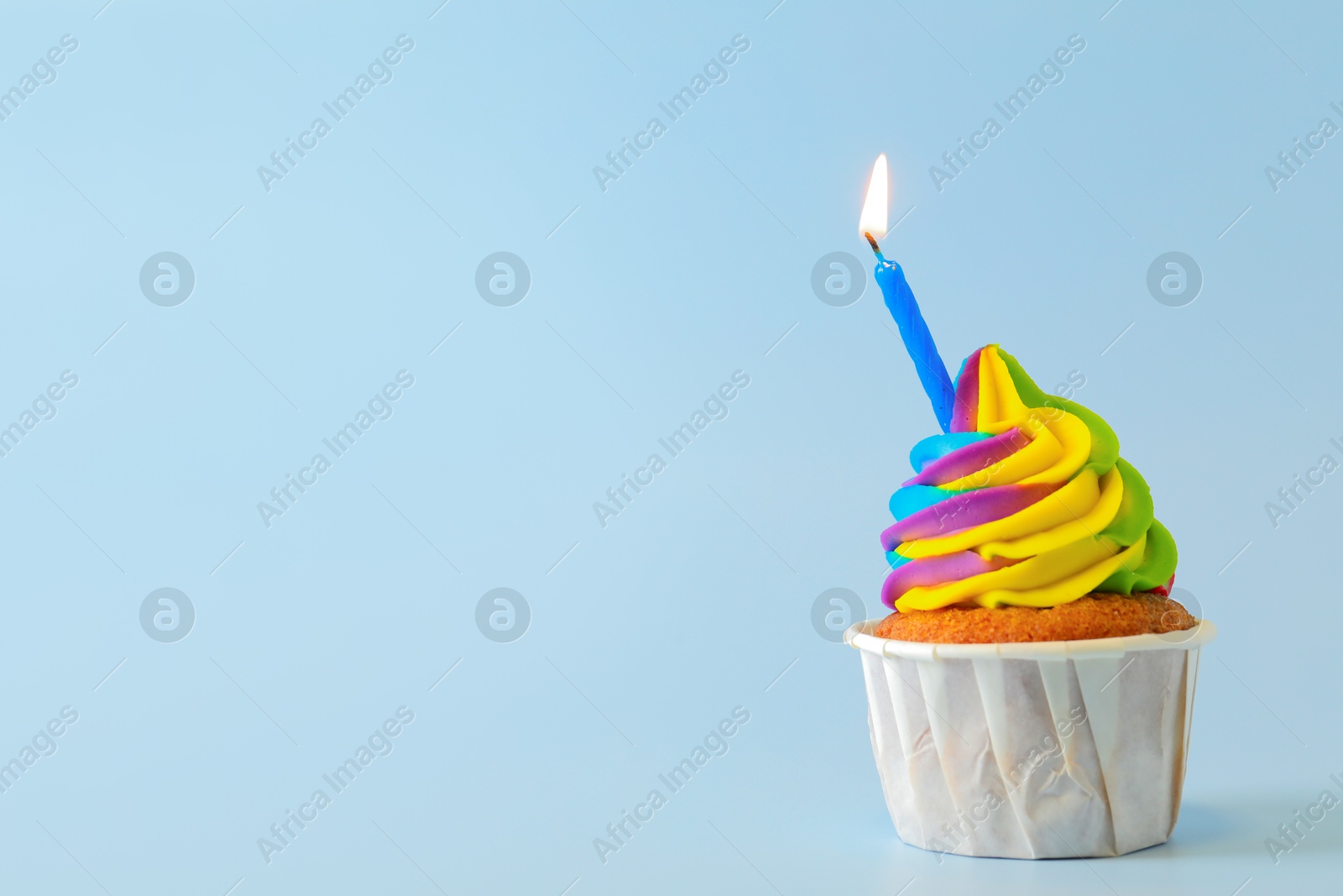 Photo of Tasty cupcake with colorful cream and burning candle on light blue background, space for text