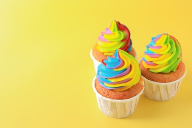 Photo of Tasty cupcakes with colorful cream on yellow background, closeup. Space for text