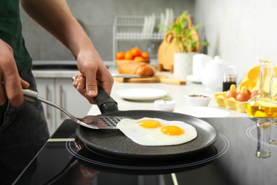 Photo of Man taking fried eggs from frying pan in kitchen, closeup