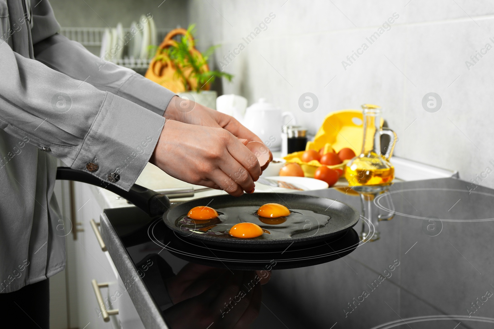 Photo of Woman breaking egg into frying pan in kitchen, closeup