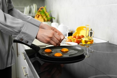 Woman breaking egg into frying pan in kitchen, closeup