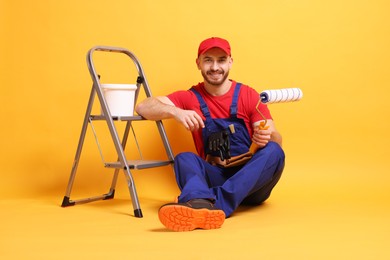 Professional painter with tools and supplies on orange background