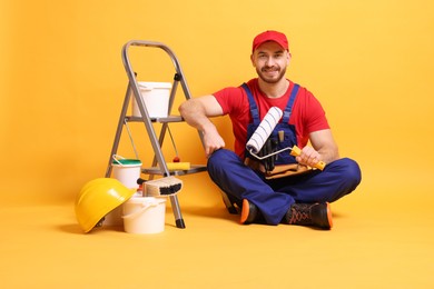 Professional painter with tools and supplies on orange background