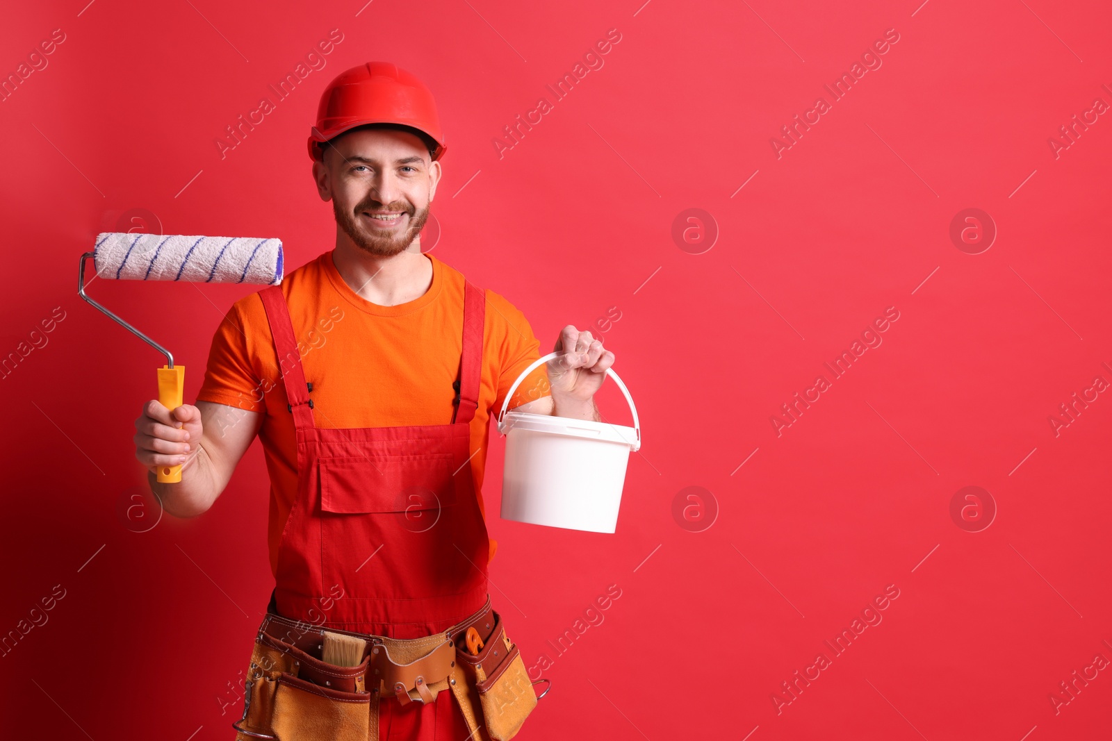 Photo of Professional painter with roller and bucket of paint on red background. Space for text