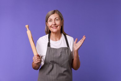 Photo of Happy woman with rolling pin on violet background