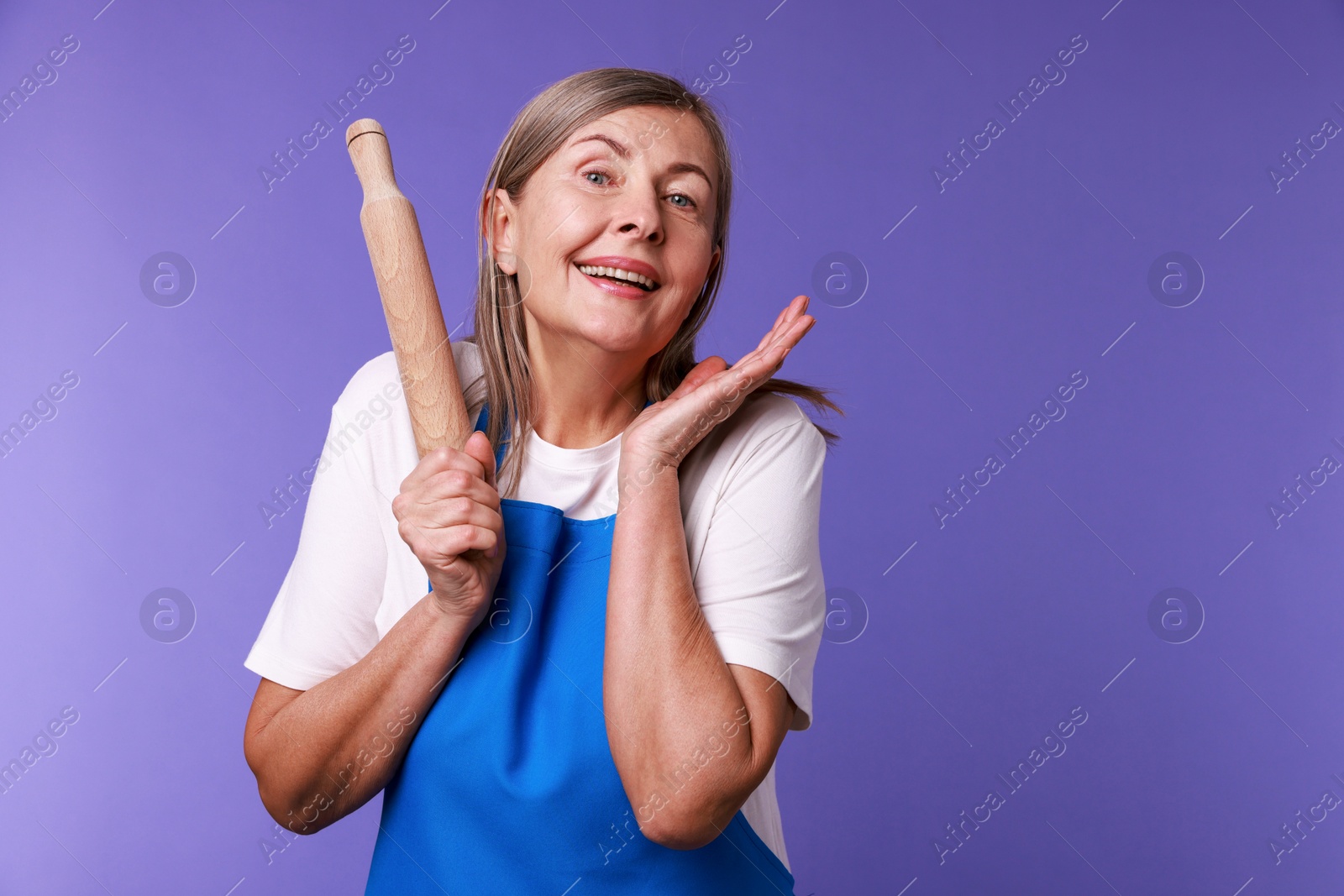 Photo of Happy woman with rolling pin on violet background. Space for text