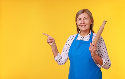 Happy woman with rolling pin pointing at something on yellow background. Space for text