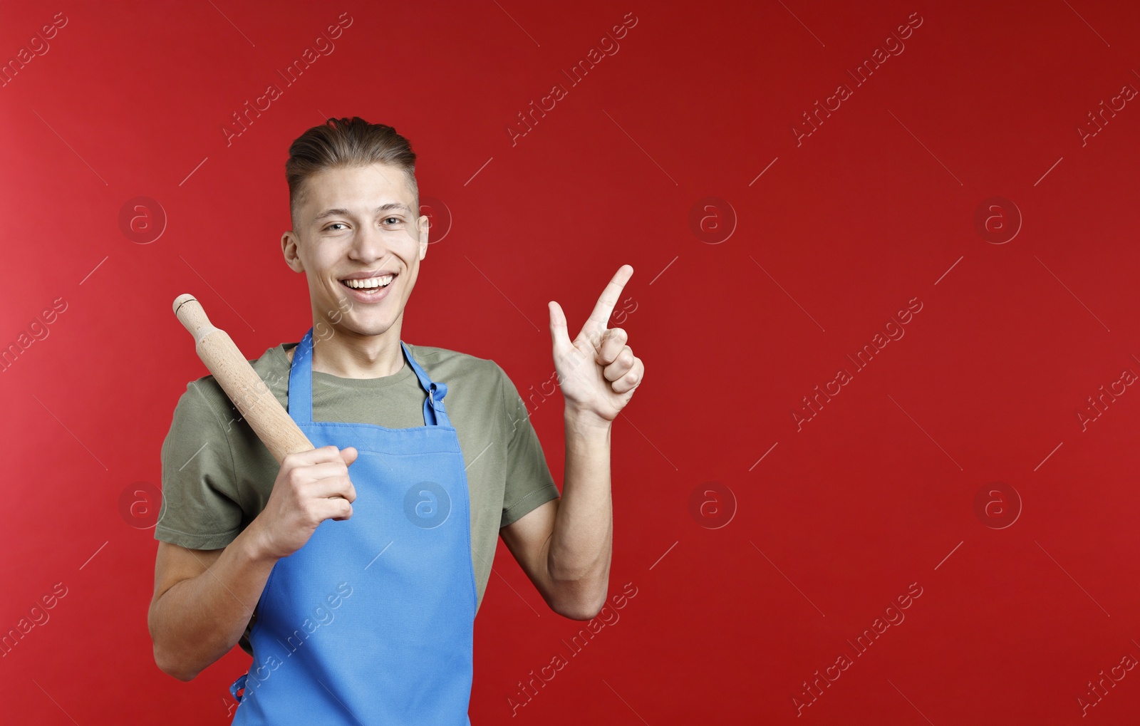 Photo of Happy man with rolling pin pointing at something on red background