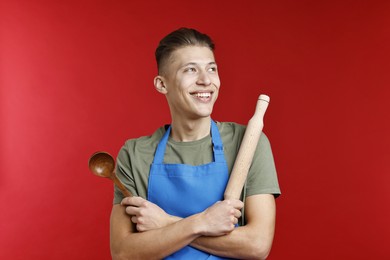 Happy man with rolling pin and spoon on red background