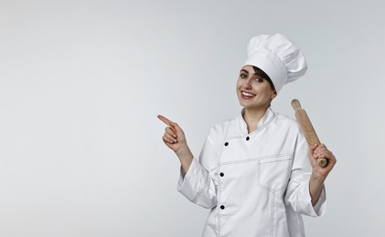 Photo of Professional chef with rolling pin pointing at something on light grey background