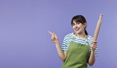 Woman with rolling pin pointing at something on violet background