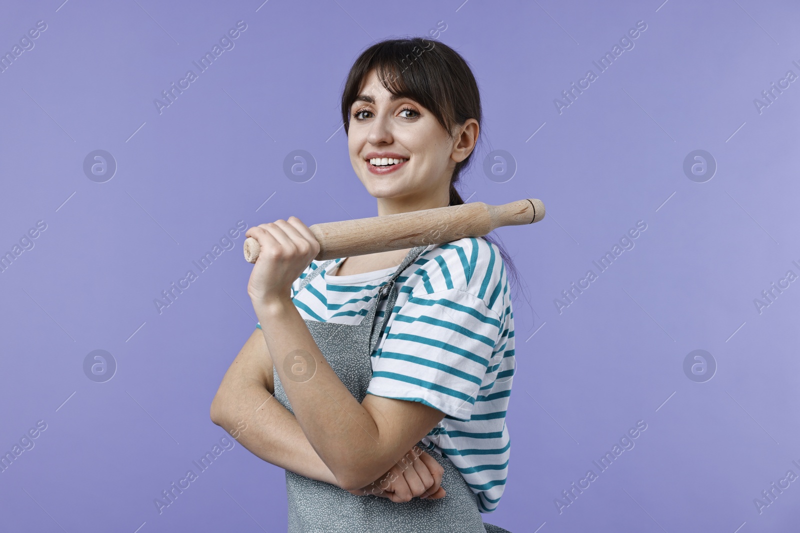 Photo of Happy woman with rolling pin on violet background