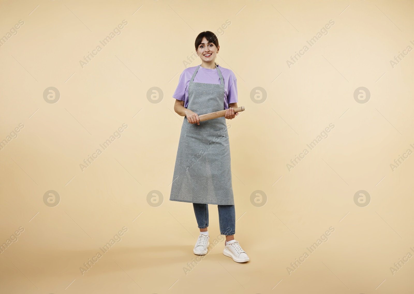 Photo of Happy woman with rolling pin on beige background