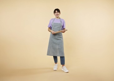 Happy woman with rolling pin on beige background