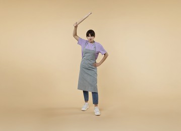 Angry woman with rolling pin on beige background