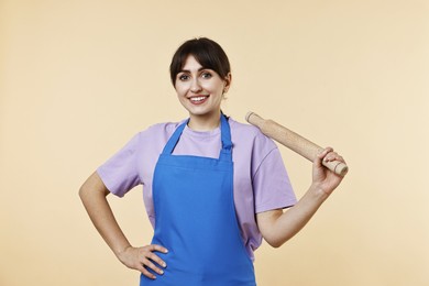 Happy woman with rolling pin on beige background