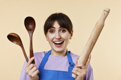 Excited woman with kitchen utensils on beige background