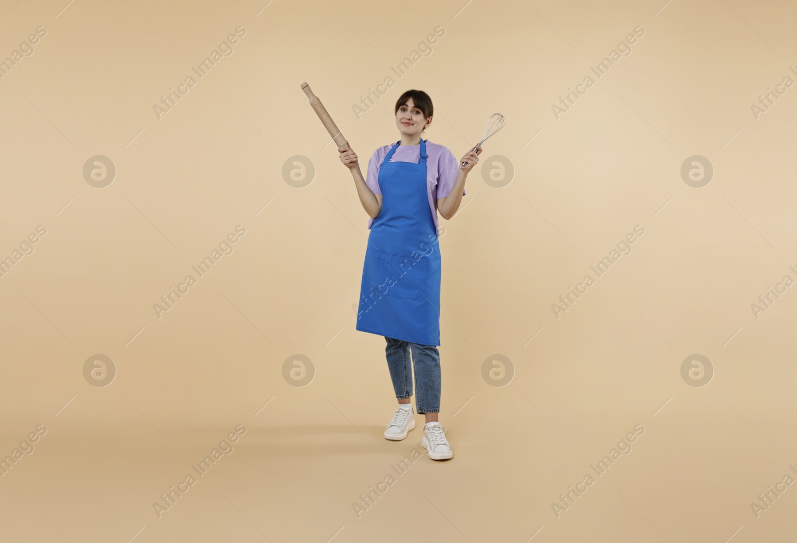 Photo of Woman with rolling pin and whisk on beige background