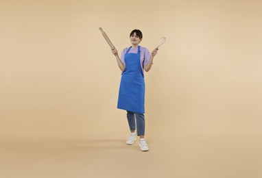 Photo of Woman with rolling pin and whisk on beige background