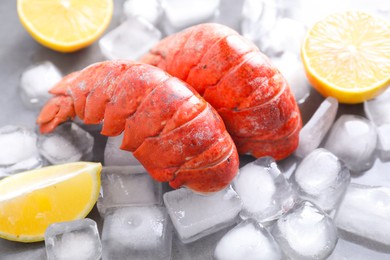 Tails of boiled lobsters with ice cubes and lemon pieces on grey table, closeup