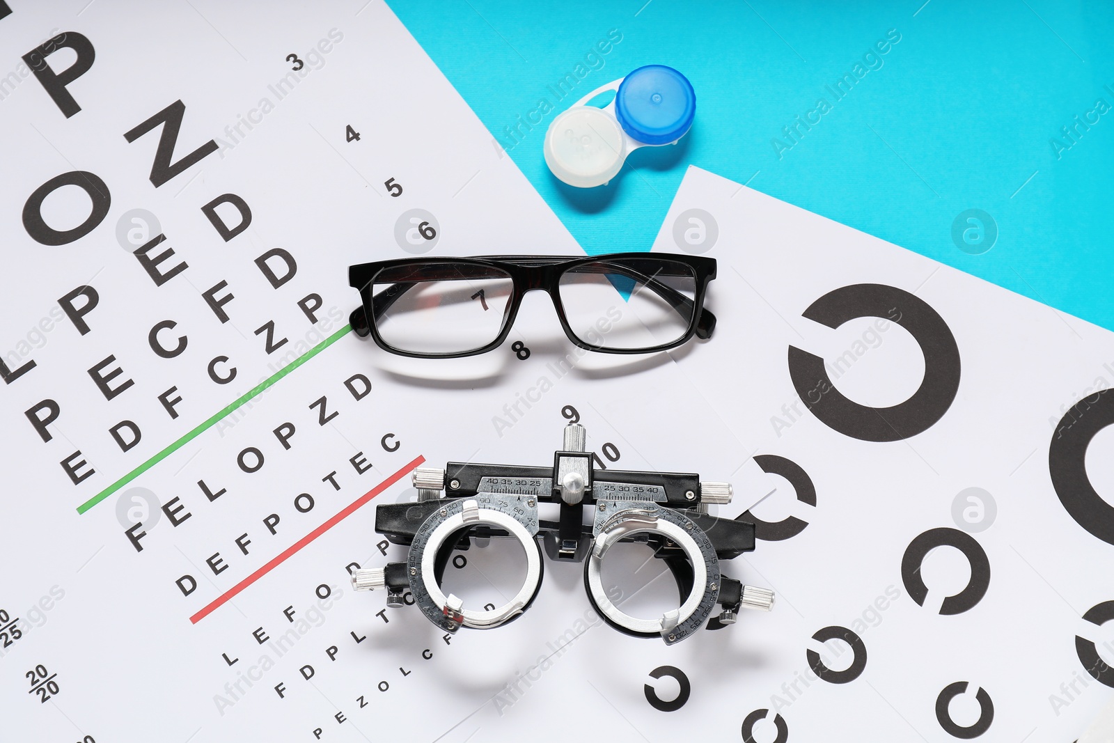 Photo of Glasses, trial frame, vision test chart and lenses on light blue background, flat lay