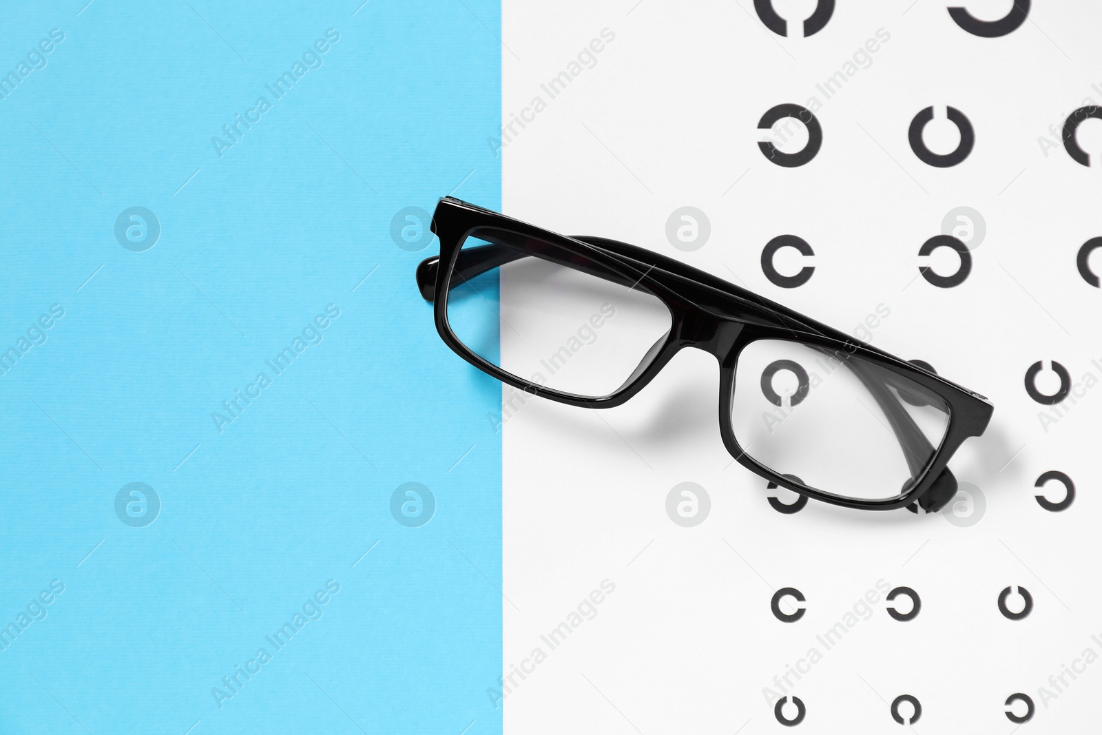 Photo of Glasses and vision test chart on light blue background, top view. Space for text