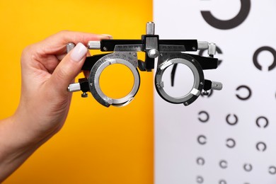 Photo of Woman holding trial frame against vision test chart on orange background, closeup