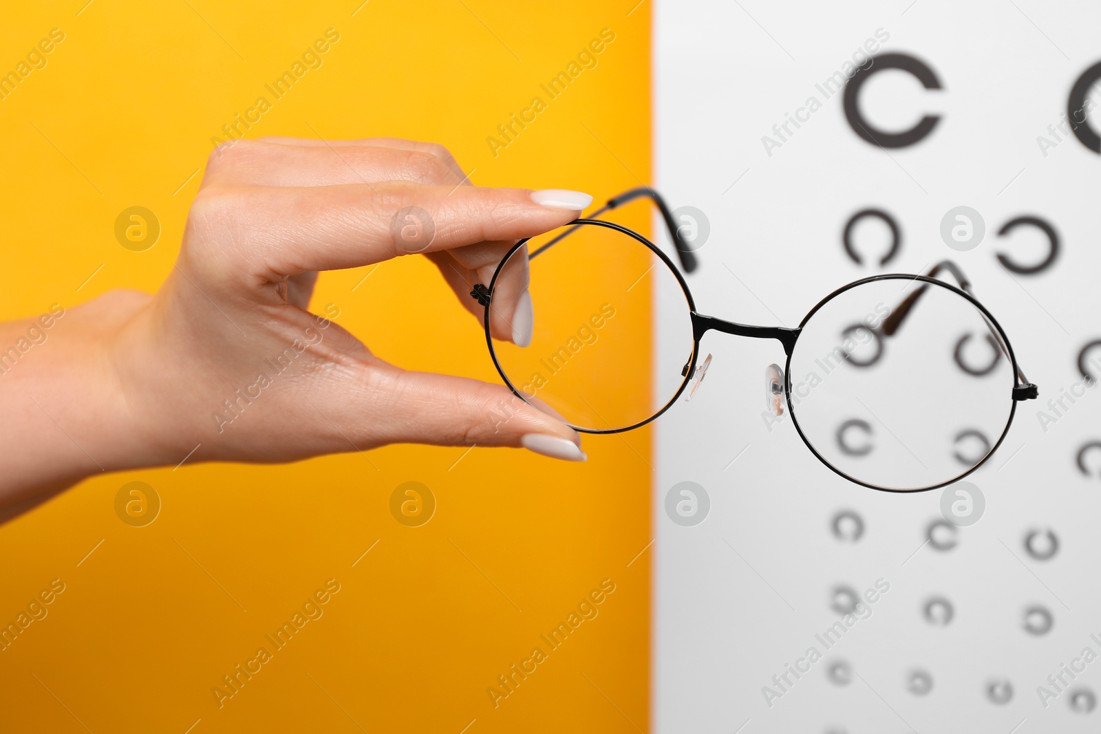 Photo of Woman holding glasses against vision test chart on orange background, closeup