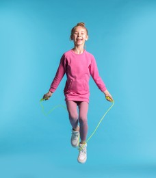 Photo of Cute little girl with jump rope on light blue background