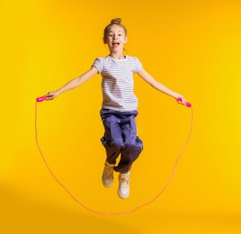 Photo of Cute little girl with jump rope on orange background