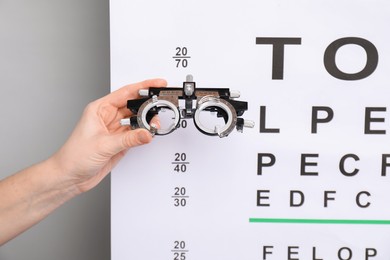 Photo of Woman holding trial frame against vision test chart on gray background, closeup