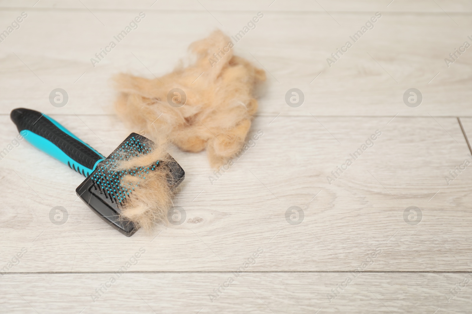 Photo of Grooming brush and pile of pet's hair on wooden floor. Space for text