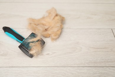 Photo of Grooming brush and pile of pet's hair on wooden floor. Space for text