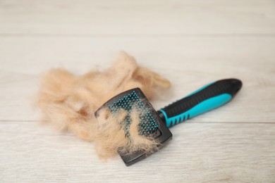 Photo of Grooming brush and pile of pet's hair on wooden floor, closeup