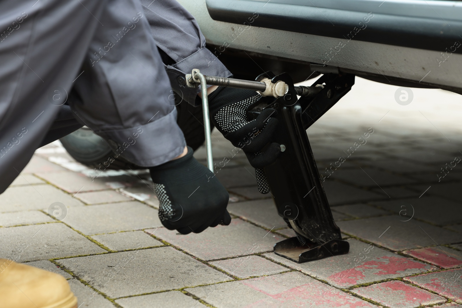 Photo of Auto mechanic lifting car with scissor jack outdoors, closeup