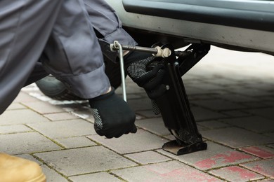 Photo of Auto mechanic lifting car with scissor jack outdoors, closeup