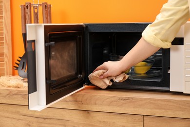 Photo of Woman cleaning microwave oven with rag indoors, closeup