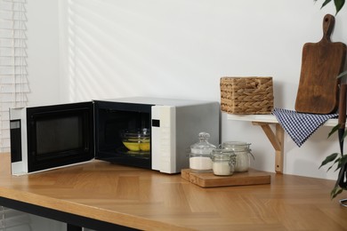 Photo of Open microwave oven with bowl of water and lemons on wooden table indoors