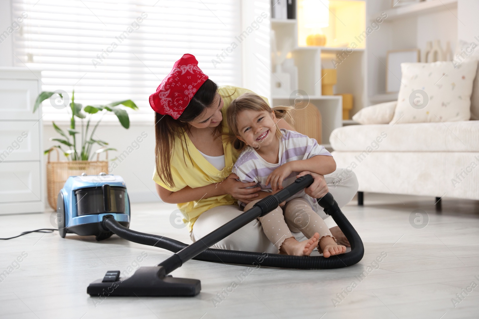 Photo of Little helper. Daughter and mother vacuuming together at home