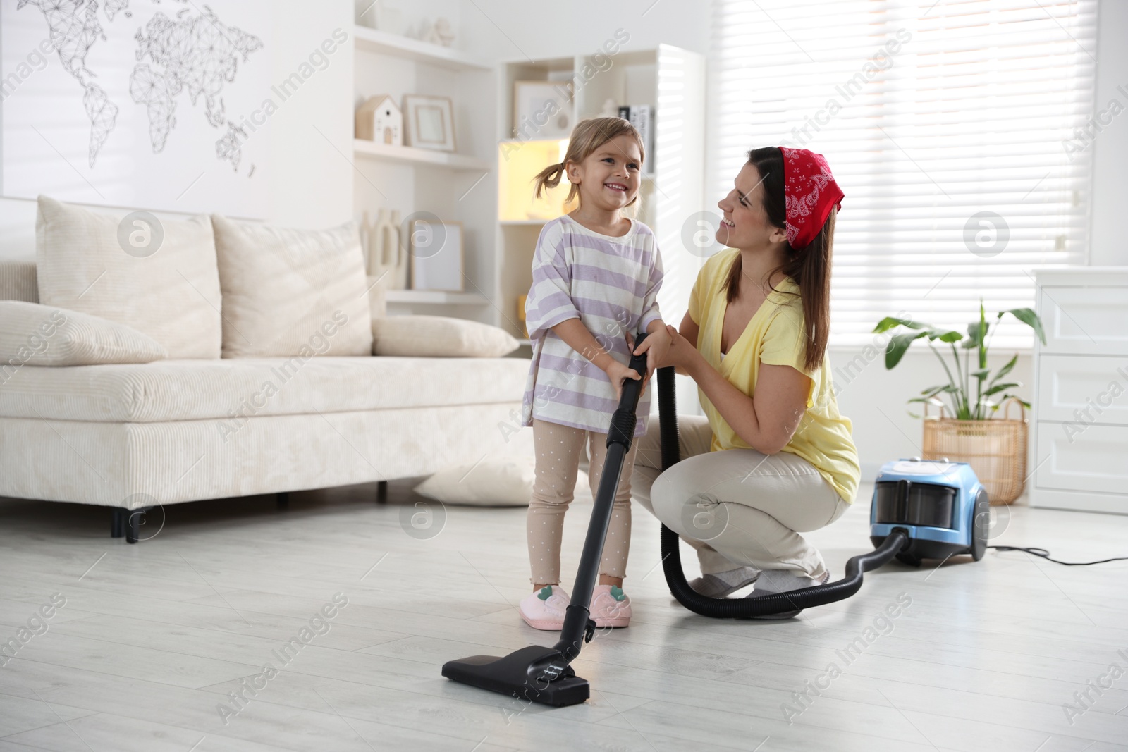 Photo of Little helper. Daughter and mother vacuuming together at home