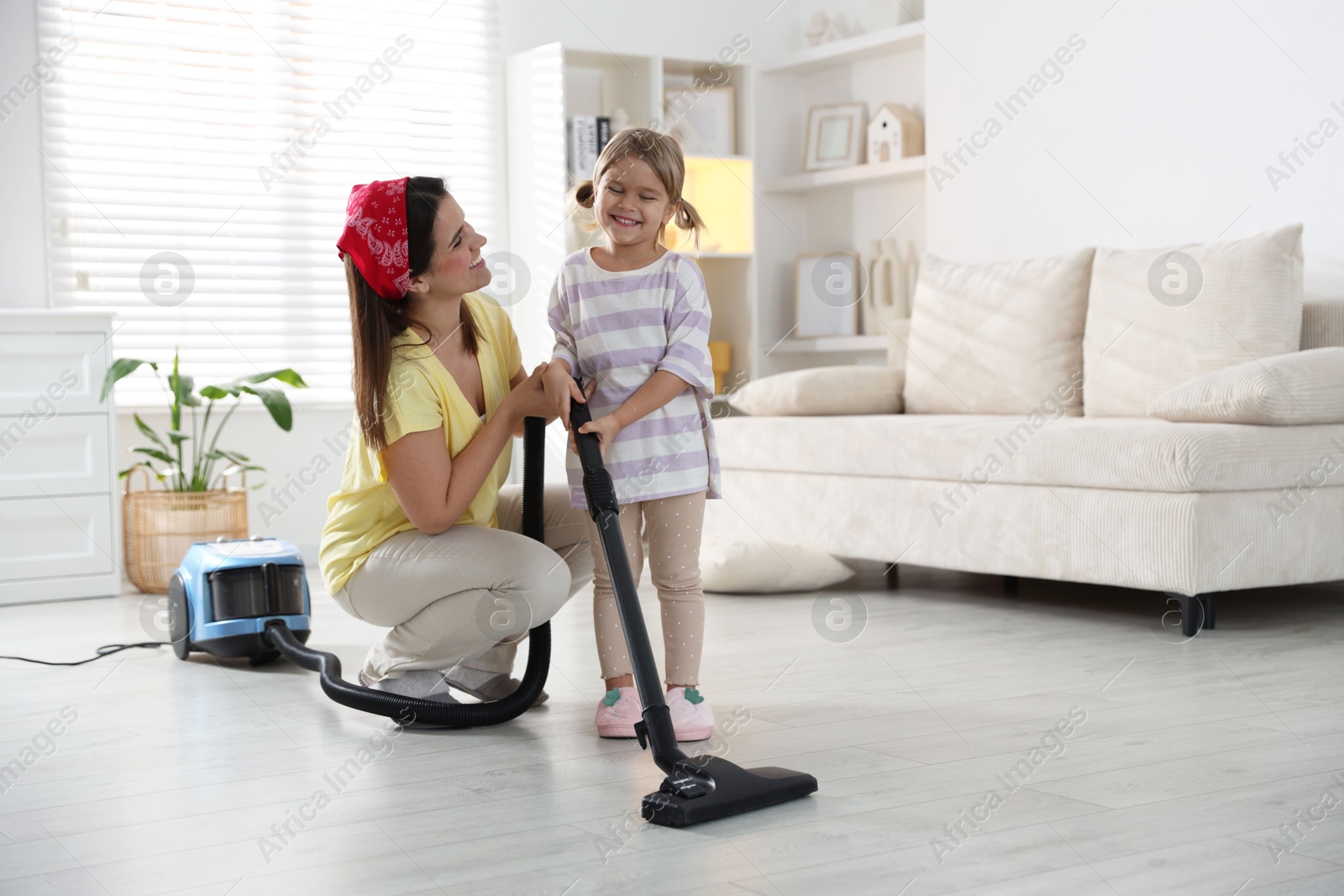 Photo of Little helper. Daughter and mother vacuuming together at home