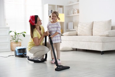 Photo of Little helper. Daughter and mother vacuuming together at home