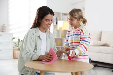 Photo of Cute little girl helping her mother wiping wooden table at home